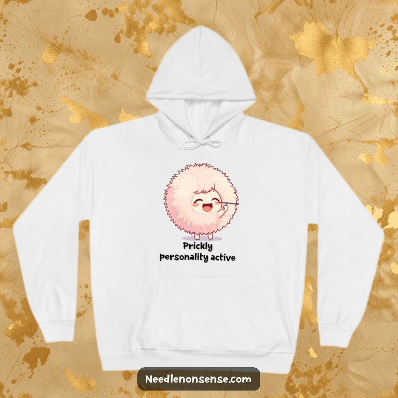Funny hoodie featuring a joyful character playfully poking a large pom-pom with a needle, offering warmth and crafting amusement.