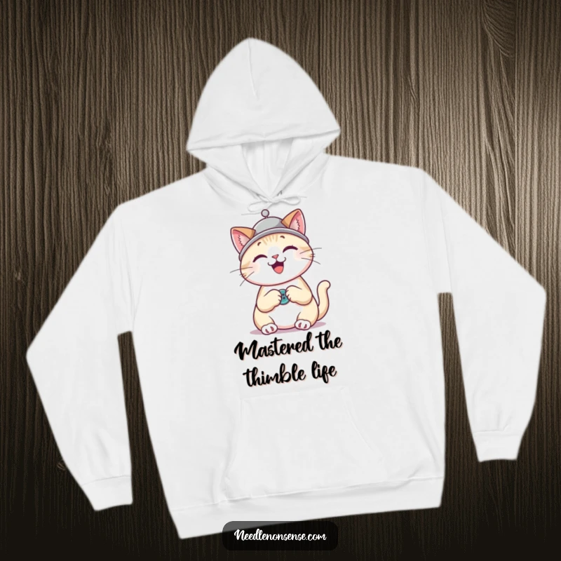 Funny cat wearing a thimble hat, happily sewing a button, depicted on a soft and cozy hoodie.