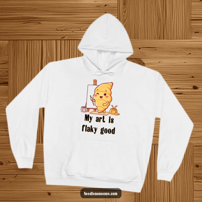 Funny hoodie featuring a cheerful croissant character preparing a canvas, combining warmth with artistic motivation.