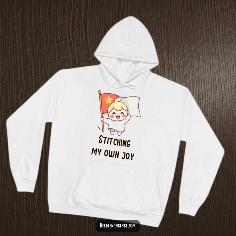 Funny hoodie depicting a cheerful character sewing a smiling face onto a waving flag, offering warmth and a dose of happy vibes.